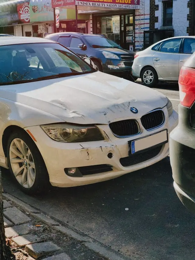 A white BMW car with car body dents.