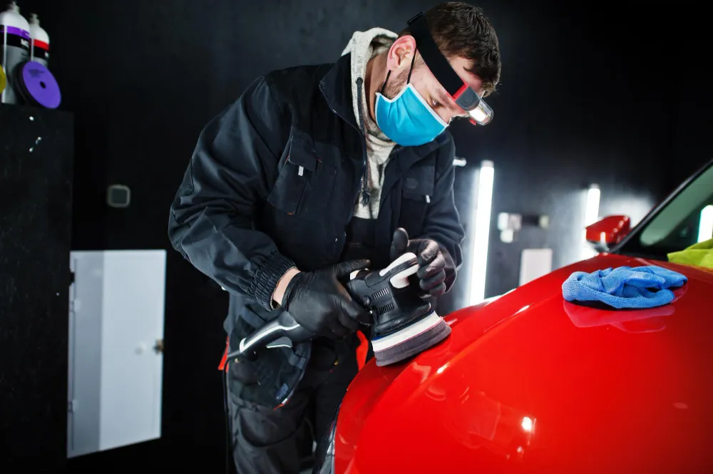 A person buffing a red car to get rid of swirl marks