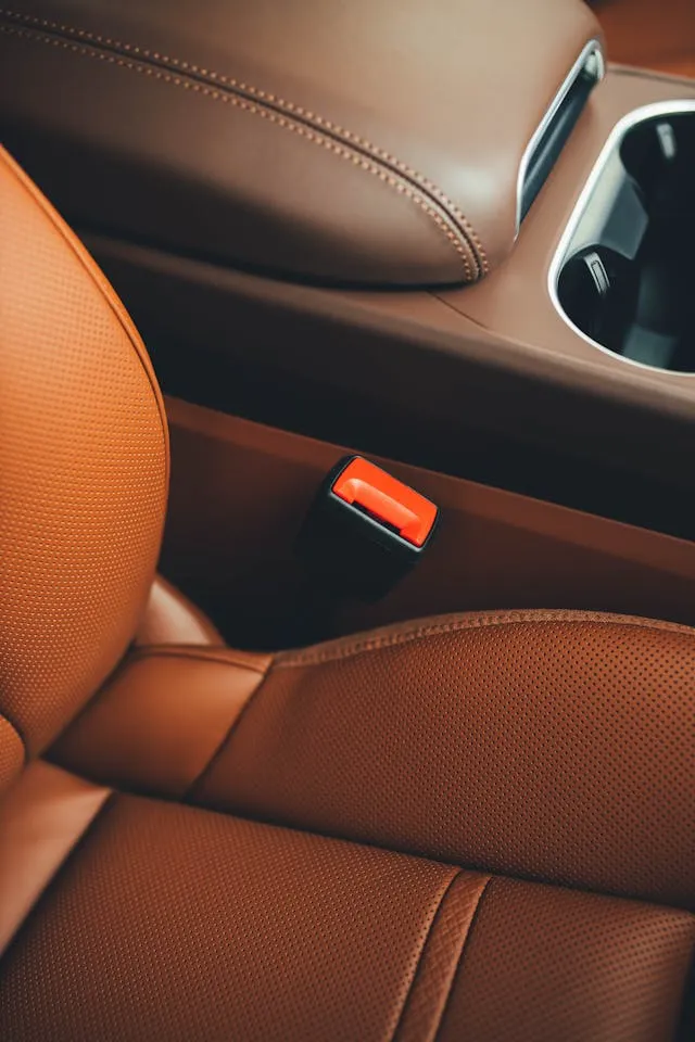 Close-up of premium tan leather car seat with red seatbelt button, showcasing clean and stain-free upholstery in a luxury vehicle interior