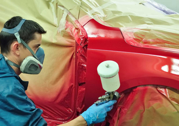 Auto technician spray painting a red car panel during the smart paint repair process