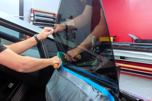 Technician applies window film to the side of the vehicle in an automotive workshop.
