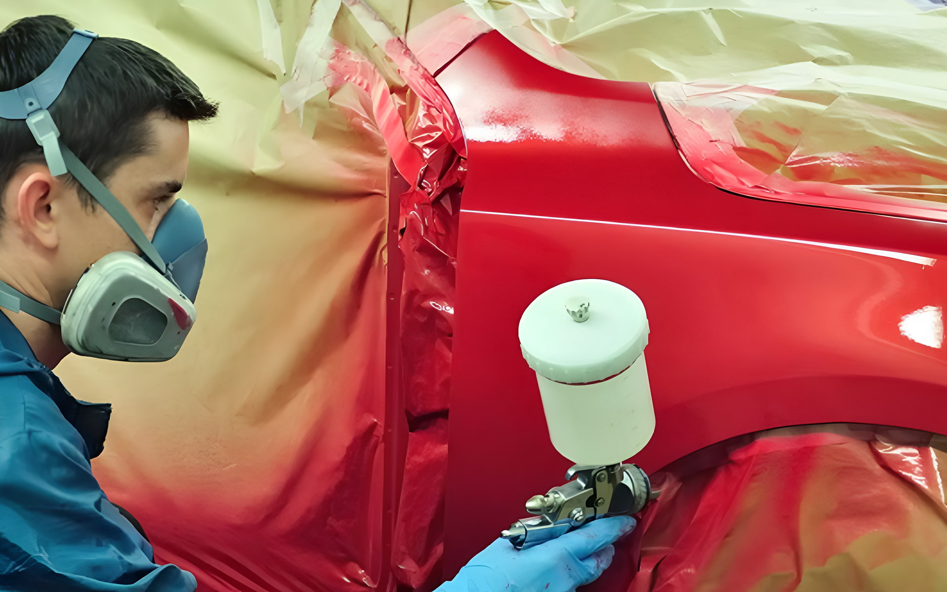 Auto body technician wearing protective gear spray painting a red car panel