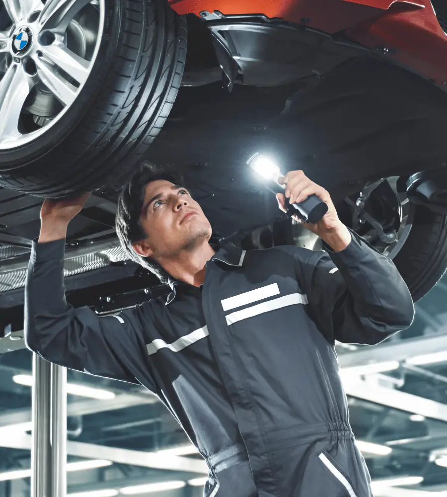 Technician inspecting the underside of a car on a lift with a work light
