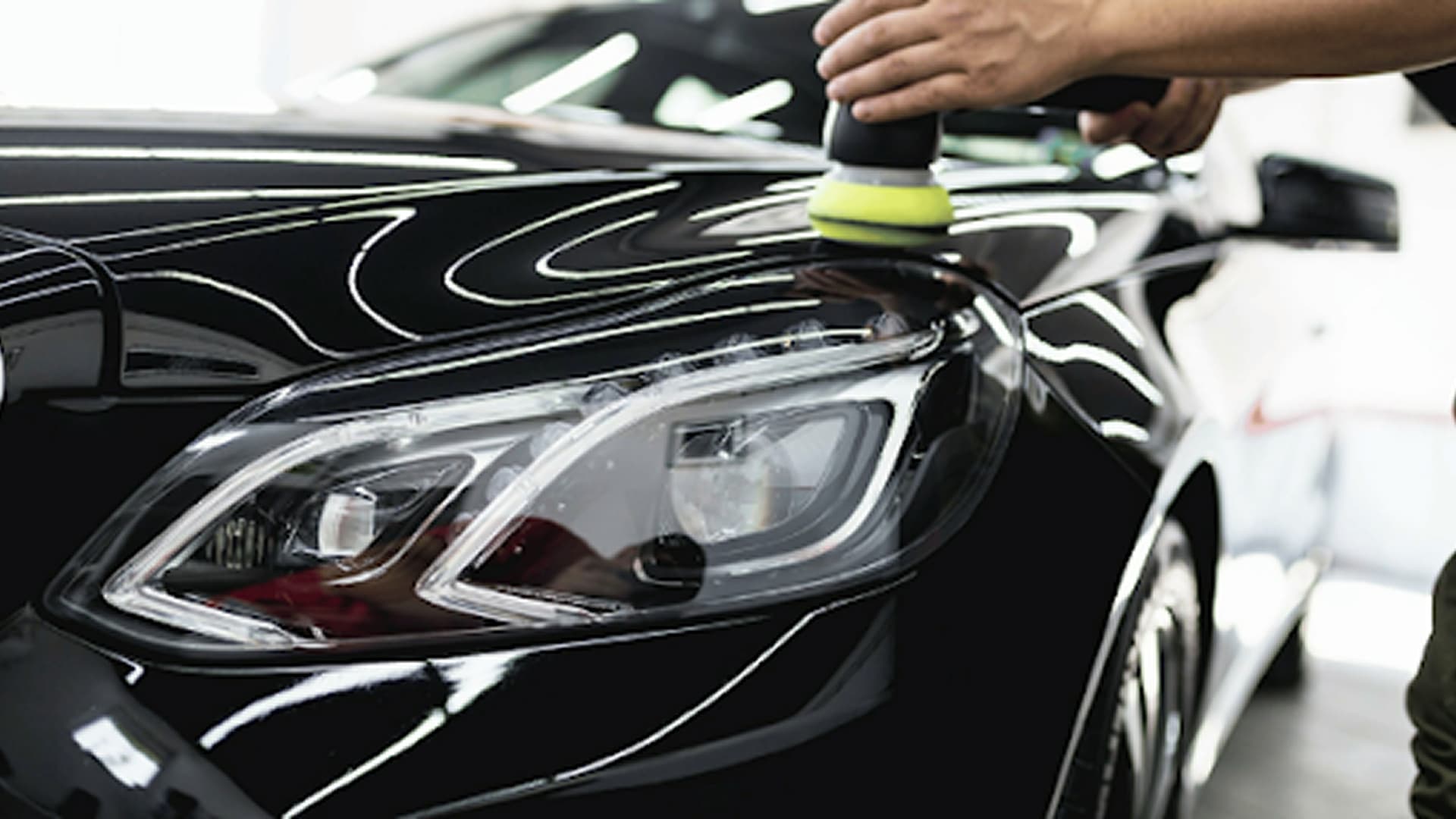 Technician machine polishing the front fender of a black car beside the headlight