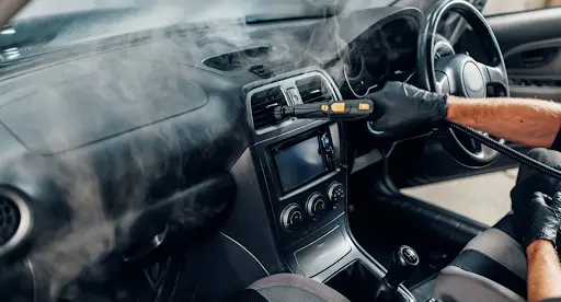 Steam cleaning the AC vents and dashboard of a car interior.