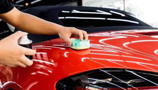 Applying fine polish by hand with a foam applicator pad to a red sports car panel