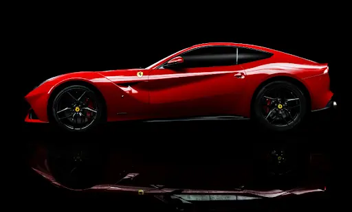 Glossy red sports car in side profile against a black studio background